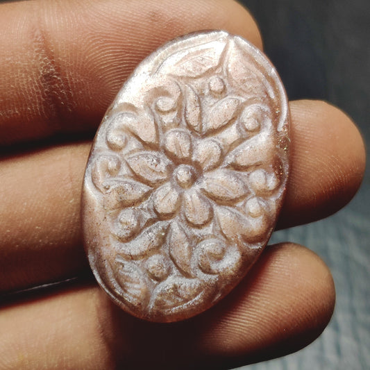 Cabochons4sale oval peach moonstone gemstone with intricate floral carving held between fingers