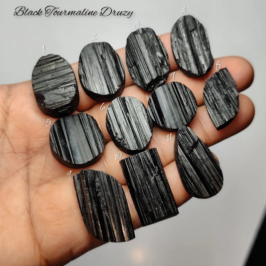 Cabochons4sale collection of raw black tourmaline druzy gemstones with natural striated textures held in a hand.