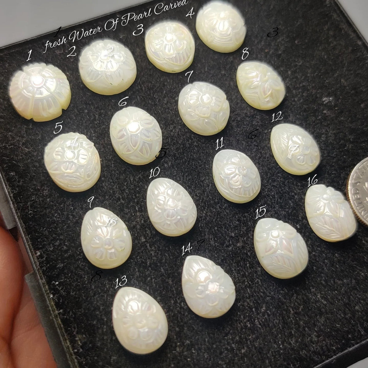 Cabochons4sale collection of white freshwater pearls hand-carved with intricate floral patterns on a black display tray