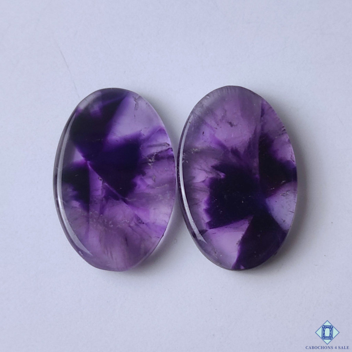 cabochons4sale, natural purple chevron amethyst oval cabochons with distinctive V-shaped quartz patterns and polished gemstone surfaces held between fingers