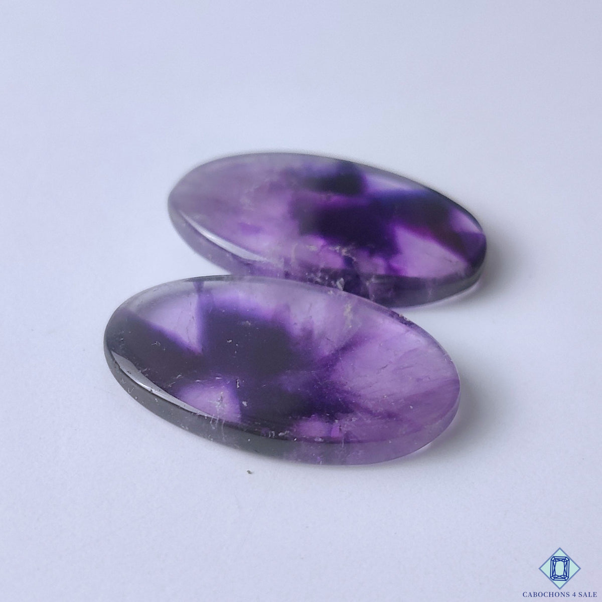 cabochons4sale, violet chevron amethyst oval cabochons showcasing natural zigzag inclusions, contrasting quartz patterns and elegant gemstone character held between fingers