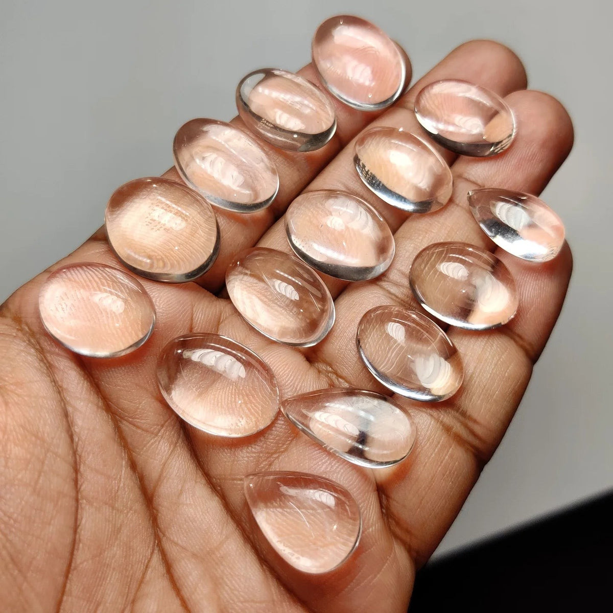Cabochons4sale clear crystal quartz gemstones in oval and teardrop shapes held in a palm for jewelry making