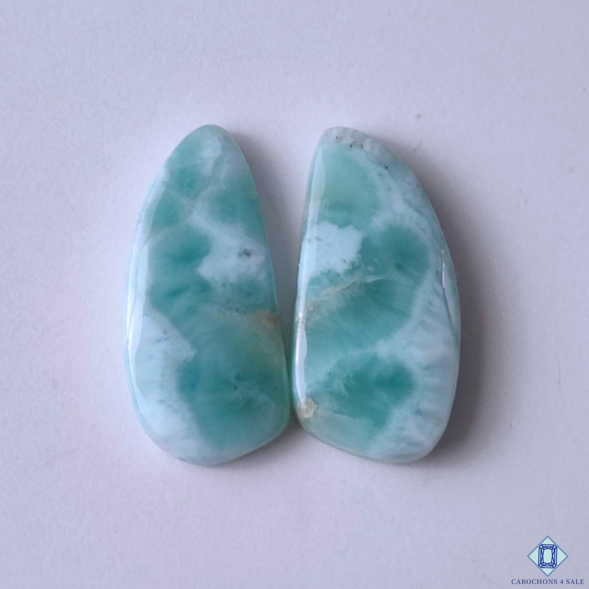 cabochons4sale, fancy larimar cabochons in blue and white shades with flowing oceanic patterns, aqua mineral tones and polished gemstone surfaces held between fingers