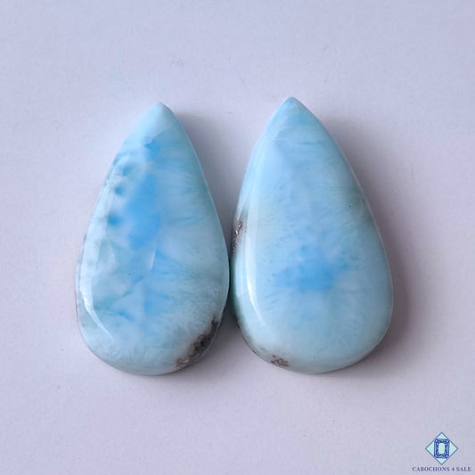 cabochons4sale, blue and white larimar pear cabochons with wave-like natural patterns, soft sky-blue hues and polished gemstone texture held between fingers