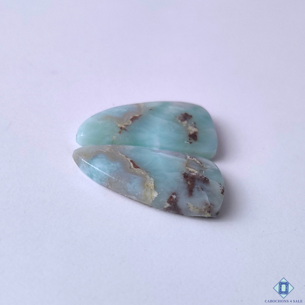 cabochons4sale, tropical-inspired fancy larimar cabochons in soft blue and white tones showcasing wave-like markings and distinctive polished stone character held between fingers