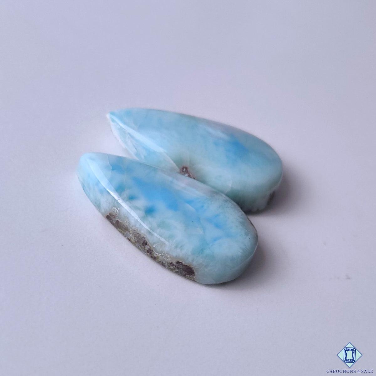 cabochons4sale, polished larimar pear cabochons in aqua blue and white shades featuring flowing ocean-inspired markings and unique natural stone character held between fingers