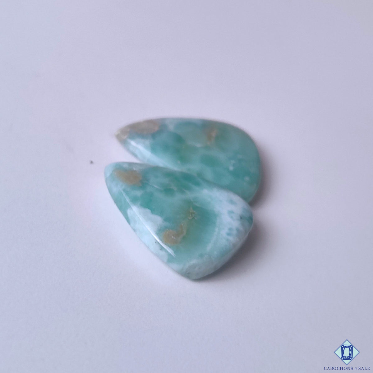 cabochons4sale, polished larimar pear cabochons in blue and white shades featuring marbled ocean-like markings, organic mineral depth and natural gemstone character held between fingers