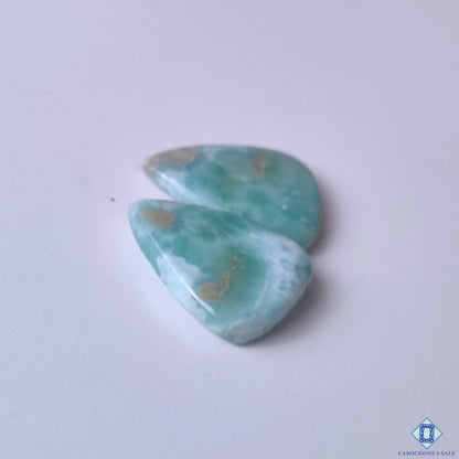 cabochons4sale, polished larimar pear cabochons in blue and white shades featuring marbled ocean-like markings, organic mineral depth and natural gemstone character held between fingers