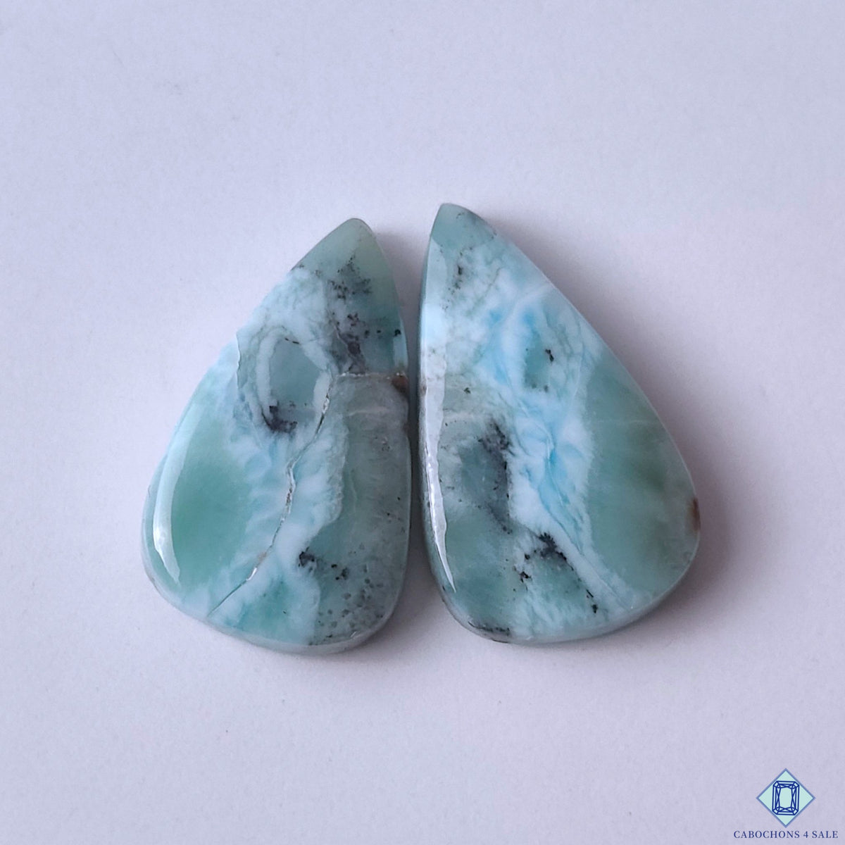 cabochons4sale, natural blue and white larimar pear cabochons with ocean-like patterns, soft color variation and polished gemstone surfaces held between fingers