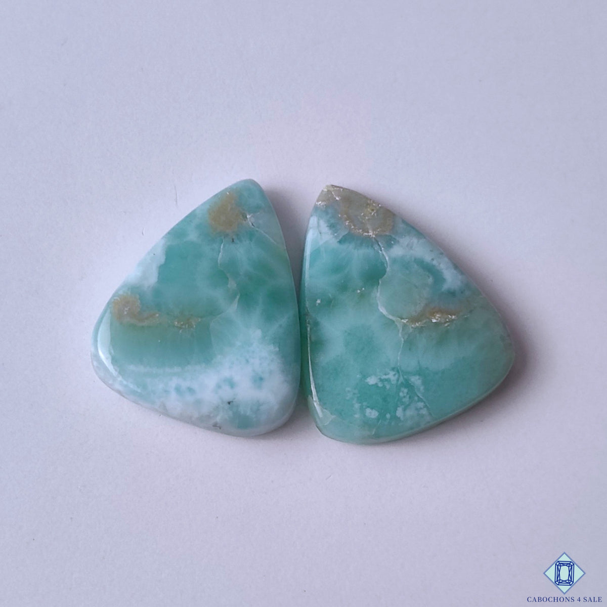 cabochons4sale, blue and white larimar pear cabochons with soft aqua tones, natural cloudy patterns and polished gemstone surfaces held between fingers