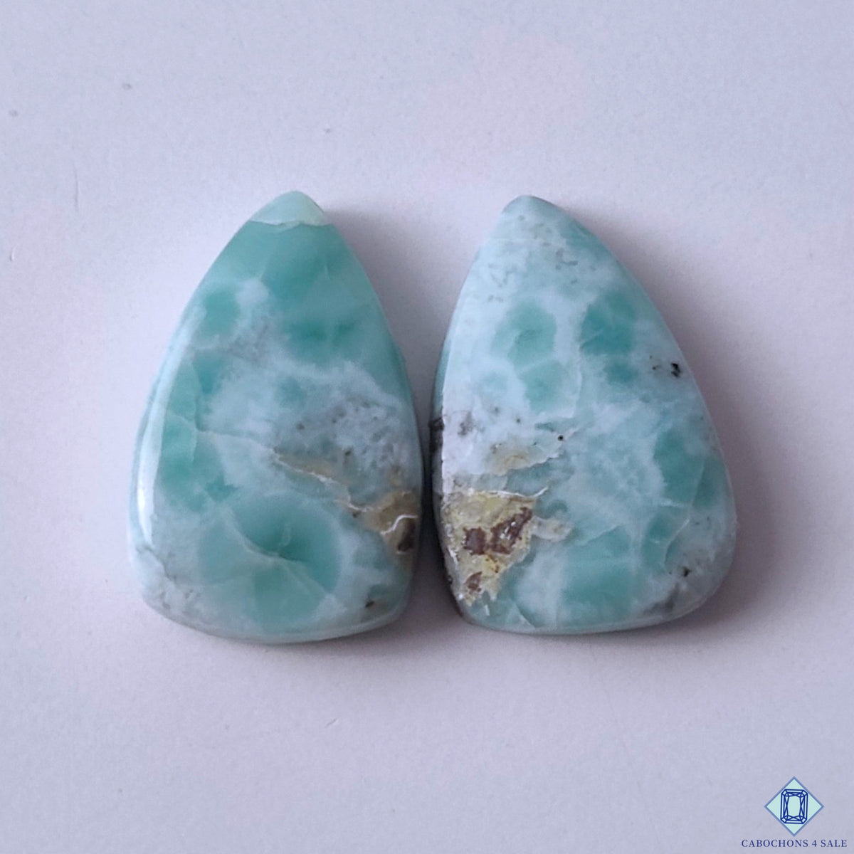 cabochons4sale, blue and white larimar pear cabochons with flowing wave patterns, aqua coloration and natural polished gemstone texture held between fingers