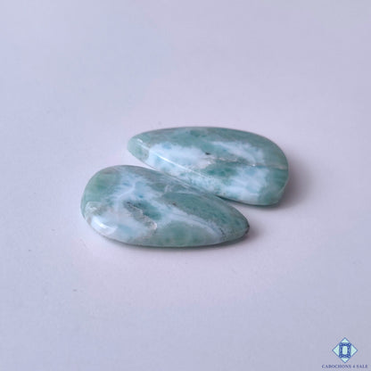cabochons4sale, tropical-inspired larimar pear cabochons in blue and white tones featuring organic wave-like markings, aqua coloration and refined gemstone polish held between fingers