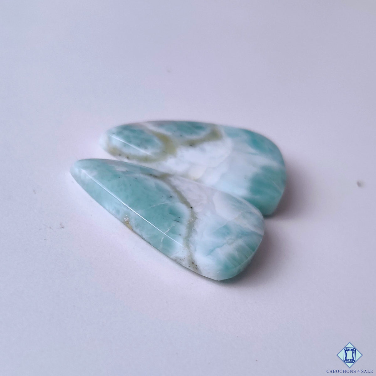 cabochons4sale, tropical blue and white larimar pear cabochons showcasing soft cloudy markings, organic mineral patterns and refined gemstone polish held between fingers