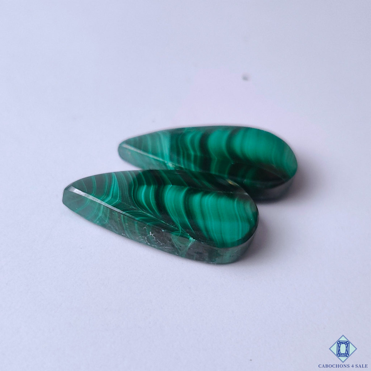 cabochons4sale, polished emerald green malachite pear cabochons showcasing layered circular markings, deep mineral tones and smooth gemstone texture held between fingers