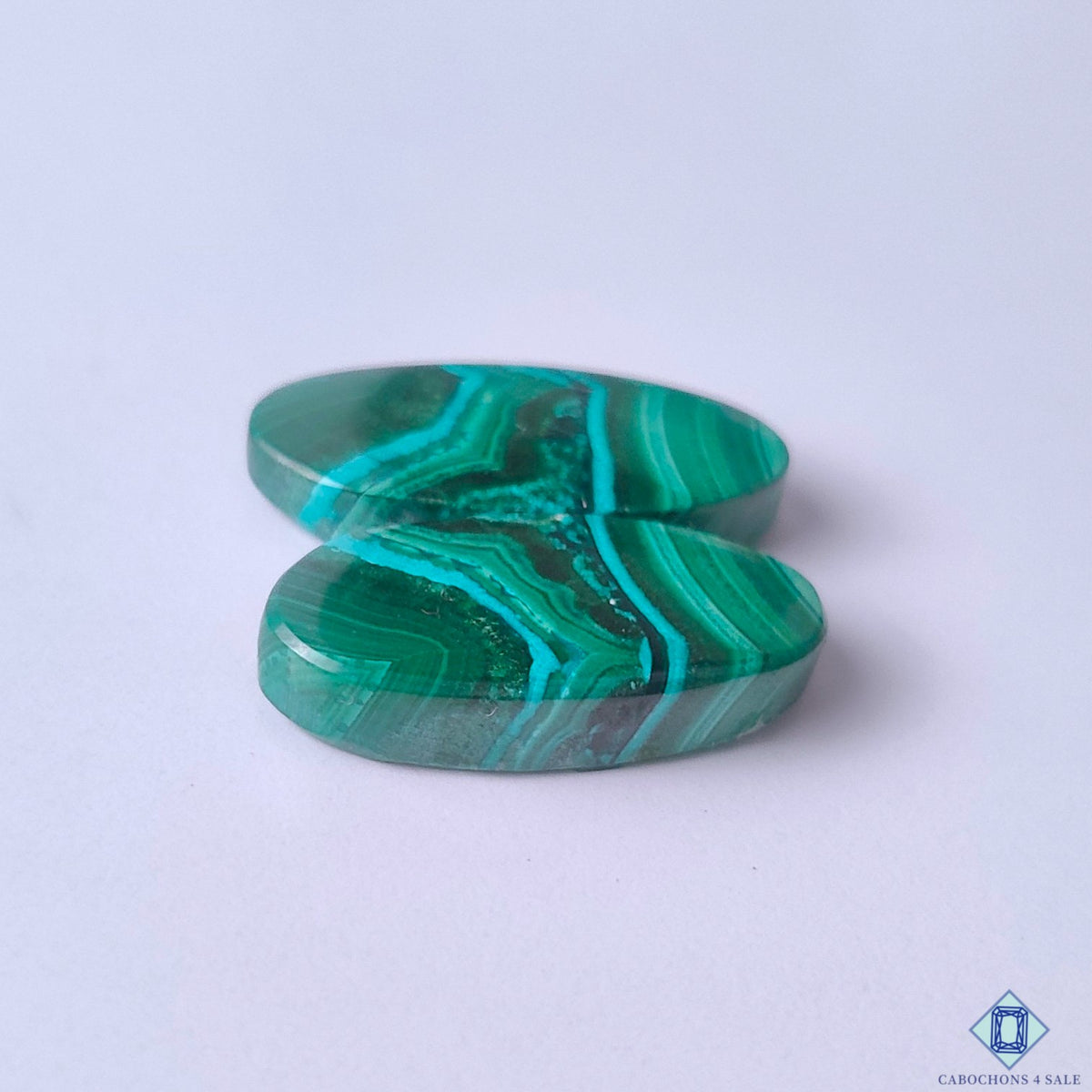 cabochons4sale, natural emerald green malachite oval cabochons showcasing distinctive banding, vibrant mineral character and artisan-polished surfaces held between fingers