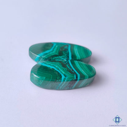 cabochons4sale, natural emerald green malachite oval cabochons showcasing distinctive banding, vibrant mineral character and artisan-polished surfaces held between fingers