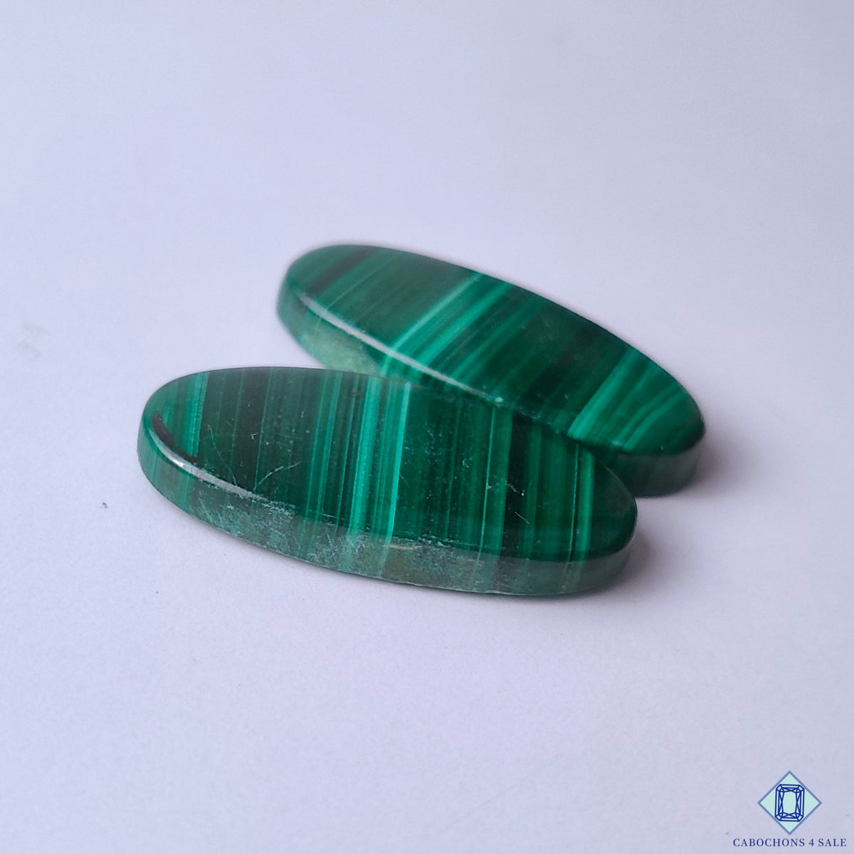 cabochons4sale, natural malachite oval cabochons in vibrant green shades showcasing organic banding, mineral depth and distinctive stone texture held between fingers