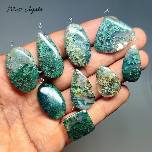 Cabochons4sale collection of natural moss agate cabochons with green dendritic inclusions held in a hand.