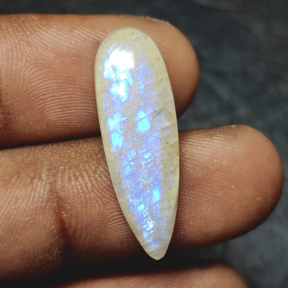 Cabochons4sale pear-shaped translucent Belomorite gemstone with blue iridescent flash held between fingers.