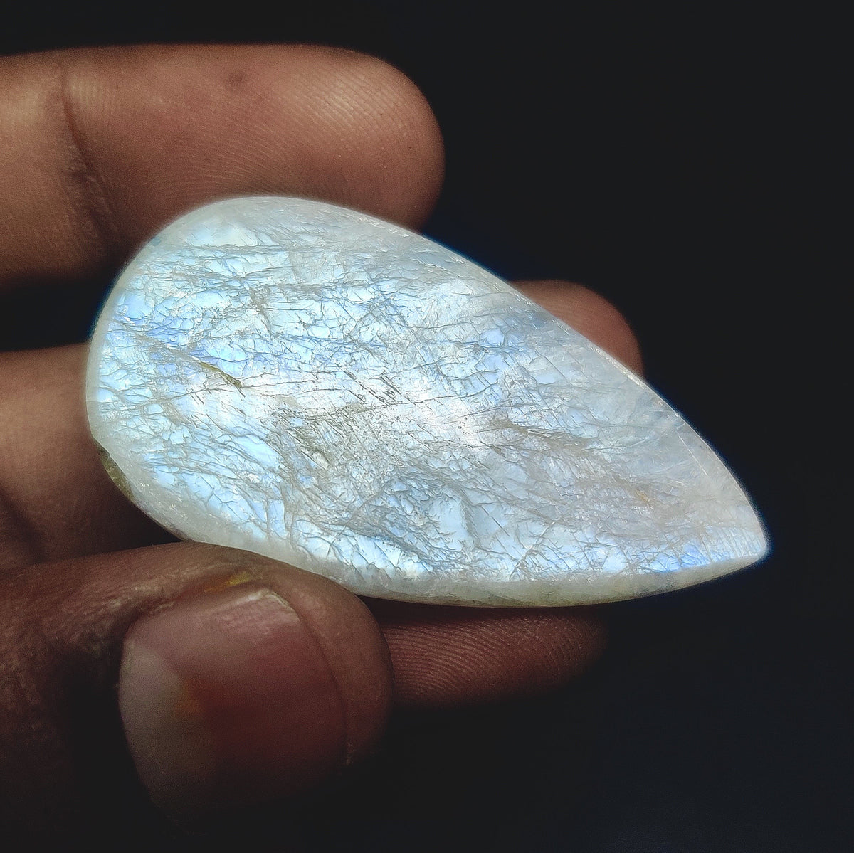 Cabochons4sale pear-shaped translucent white moonstone cabochon held between fingers showing natural inclusions