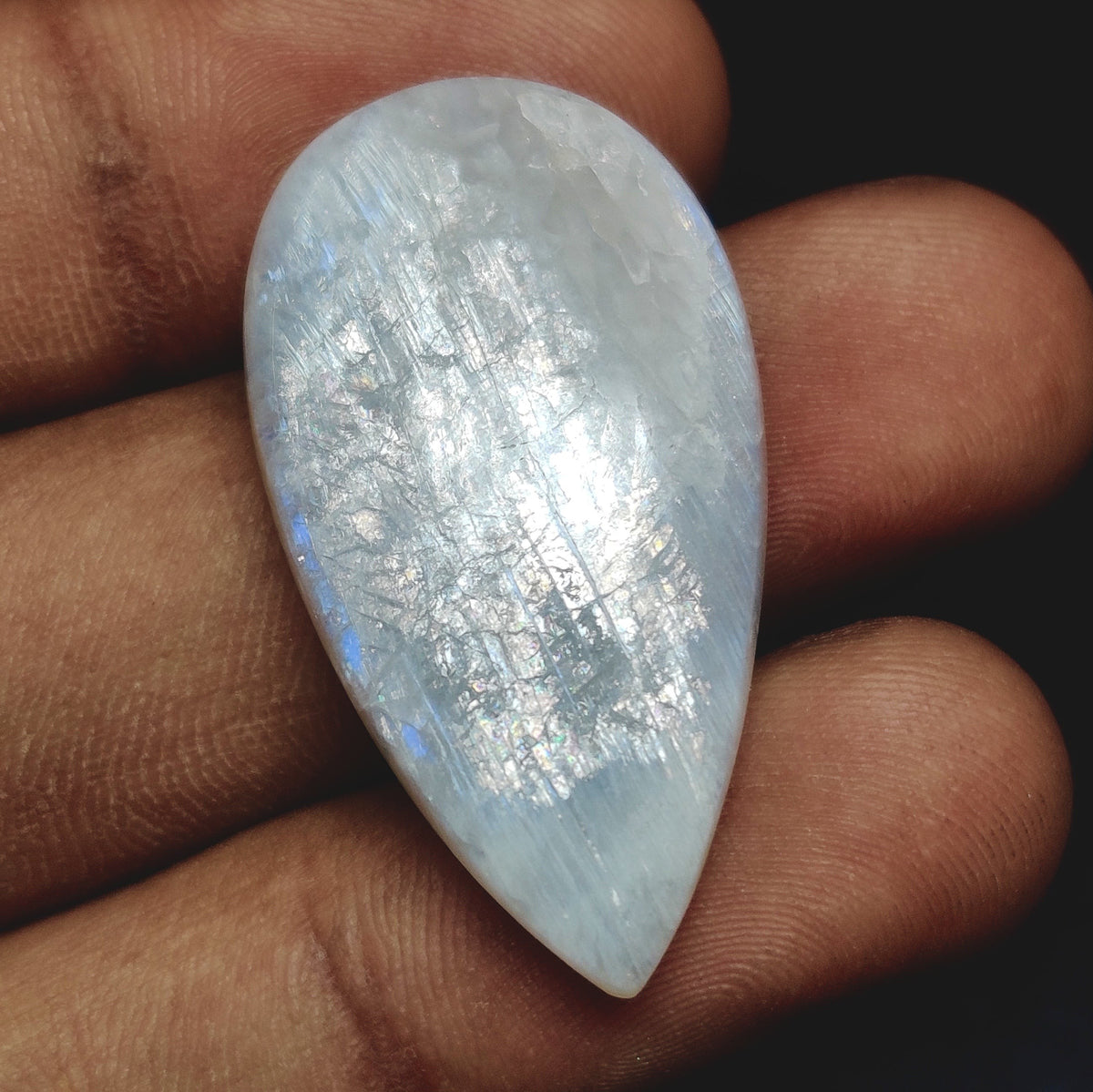 Cabochons4sale pear-shaped translucent white moonstone cabochon held in fingers showing iridescent shimmer