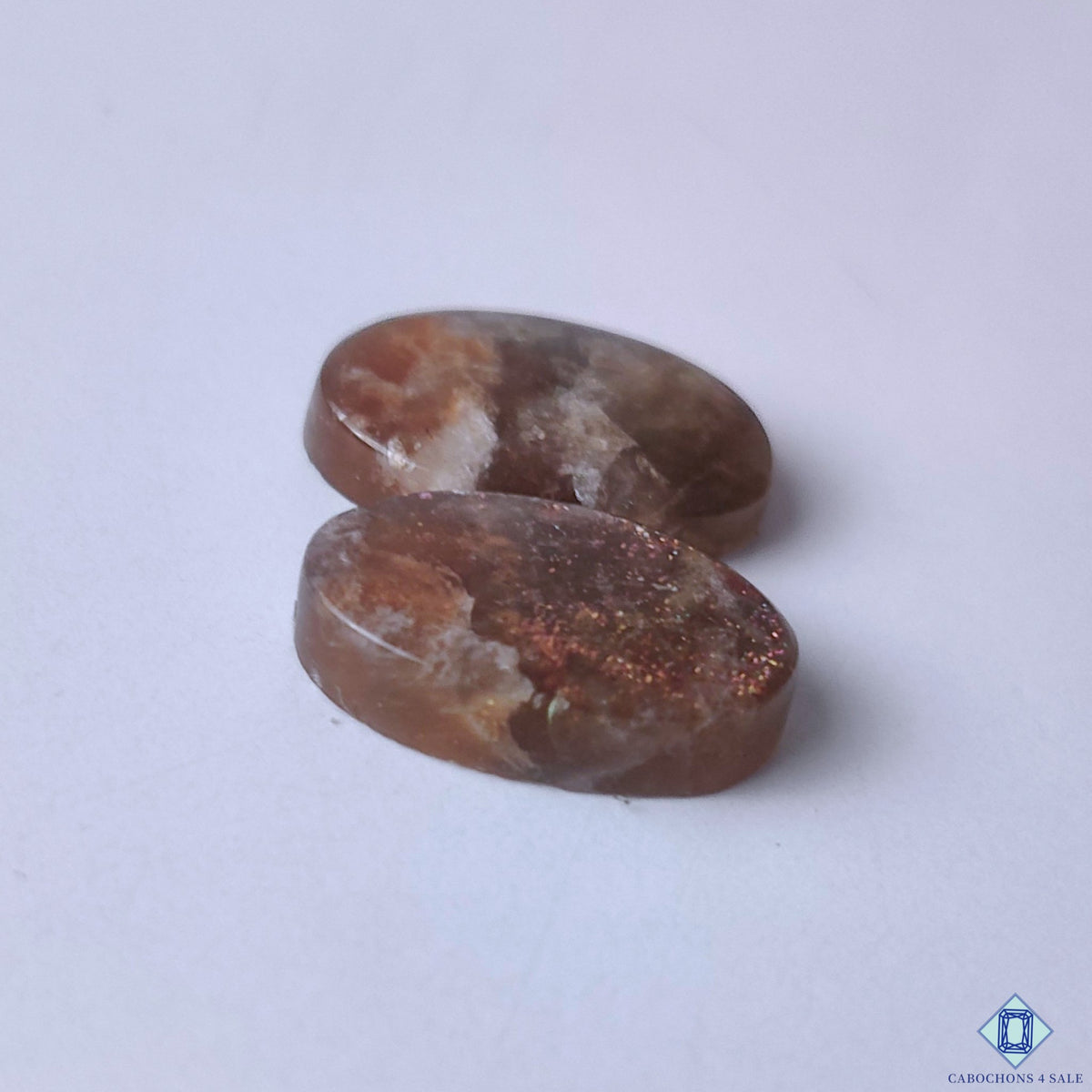 cabochons4sale, polished oval purple haze sunstone cabochons showcasing dreamy violet hues, gentle light-catching shimmer and distinctive natural gemstone character held between fingers