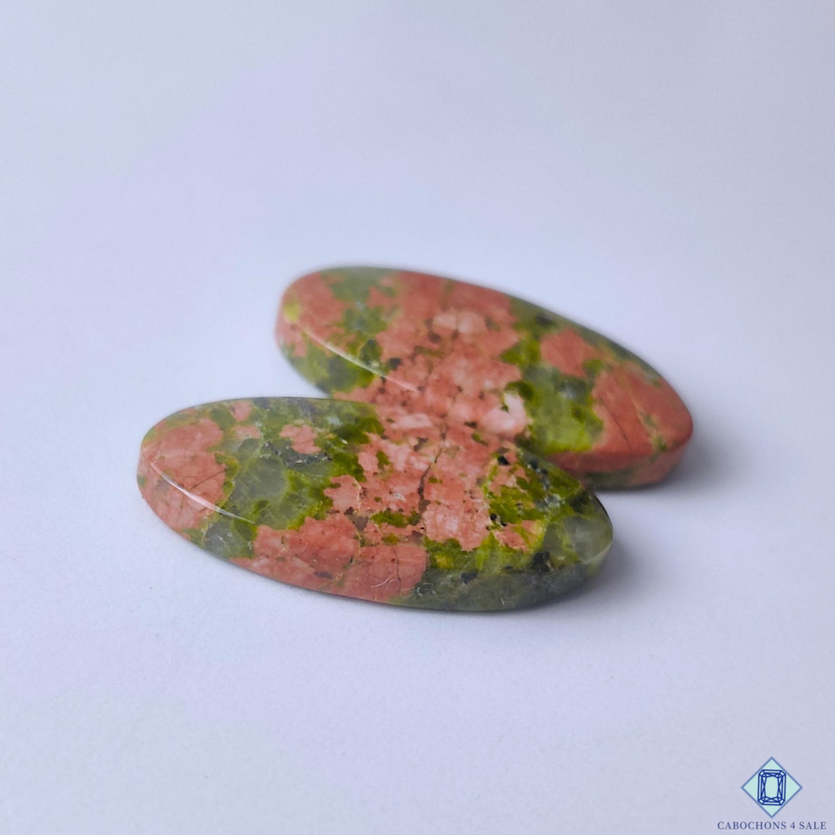cabochons4sale, oval unakite cabochons in earthy green and orange shades showcasing organic mineral textures, natural color contrast and polished stone character held between fingers
